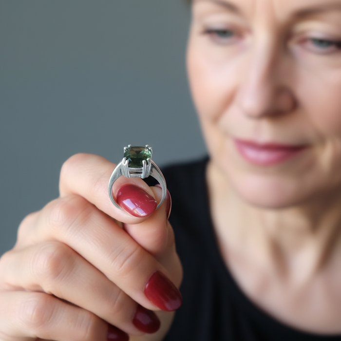 Woman holding a ring with a green moldavite gemstone against a neutral background