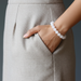 Person wearing a beige skirt with a hand in the pocket, wearing a white beaded bracelet.