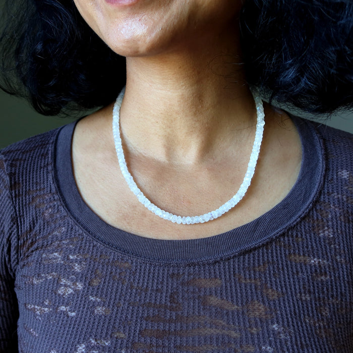 Person wearing a white beaded Rainbow Moonstone necklace with a dark textured top