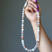 Hand holding a string of multicolored Moonstone Necklace against a gray background