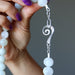 Close-up of a hand holding a White Moonstone Necklace with a silver spiral pendant against a dark background.