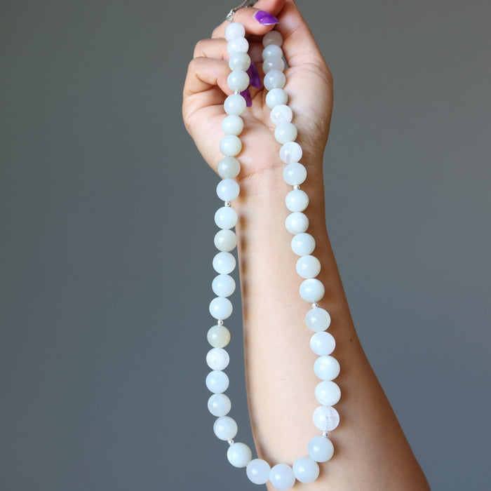 Hand holding a long White Moonstone Necklace against a gray background