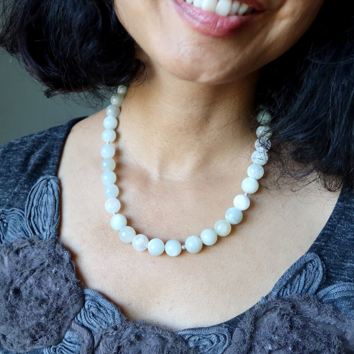 Close-up of a person wearing aWhite Moonstone Necklace with a dark gray top.