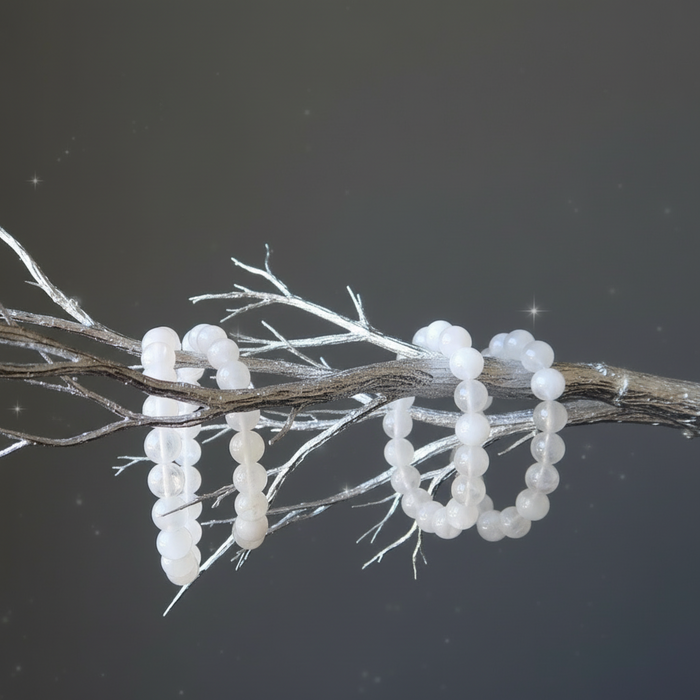 White beaded rainbow moonstone bracelets on a branch against a dark background