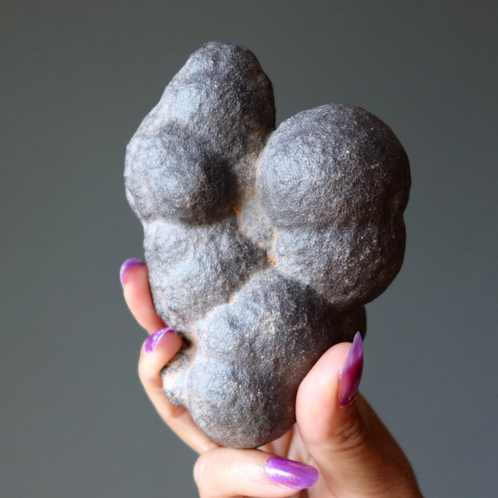 Hand holding a gray moqui marble stone with a unique shape against a gray background