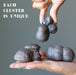 Hand holding a cluster of dark moqui marble stones with a gray background and text 'Each Cluster is Unique'.