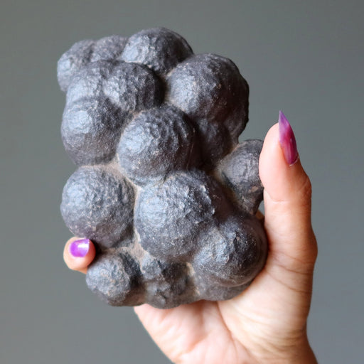 Hand holding a textured moqui marble stone against a neutral background