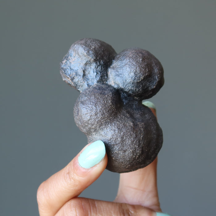 Hand holding a dark moqui marble stone against a gray background
