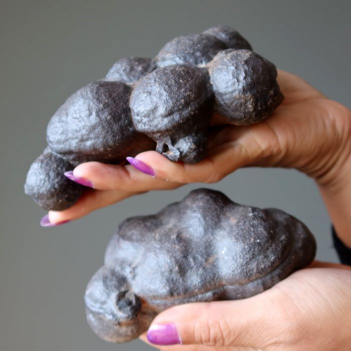 Person holding dark-colored moqui marble with a gray background
