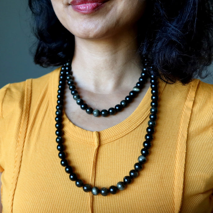 Person wearing a black Gold Sheen Obsidian beaded necklace  with a blurred background