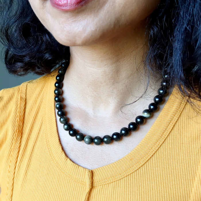 Person wearing a black Gold Sheen Obsidian beaded necklace with a blurred background