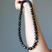 Hand holding a long black Gold Sheen Obsidian beaded necklace against a gray background