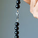 Gold Sheen Obsidian beaded necklace  with a clasp held by a hand against a gray background