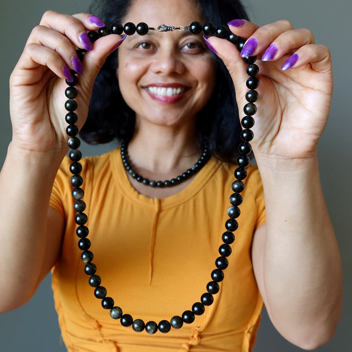 Woman holding a black Gold Sheen Obsidian beaded necklace against a gray background