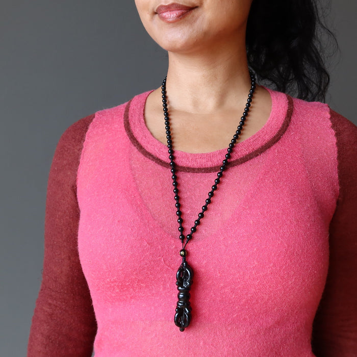 Person wearing a black beaded necklace with a pendant on a gray background