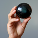 Hand holding a rainbow obsidian sphere against a neutral background