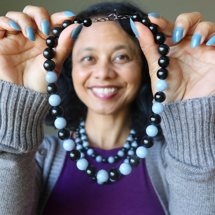 woman wearing and holding necklaces with alternating black obsidian and light blue angelite beads