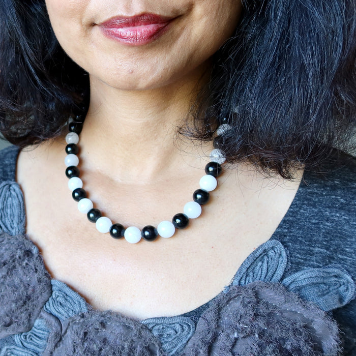 Close-up of a person wearing a black and white beaded Rainbow Obsidian Snow Quartz necklace.