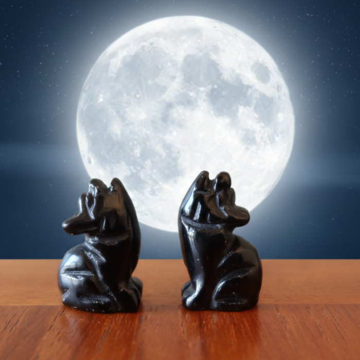 Two black obsidian stone sculptures of wolves sitting on a wooden surface with a large moon in the background.