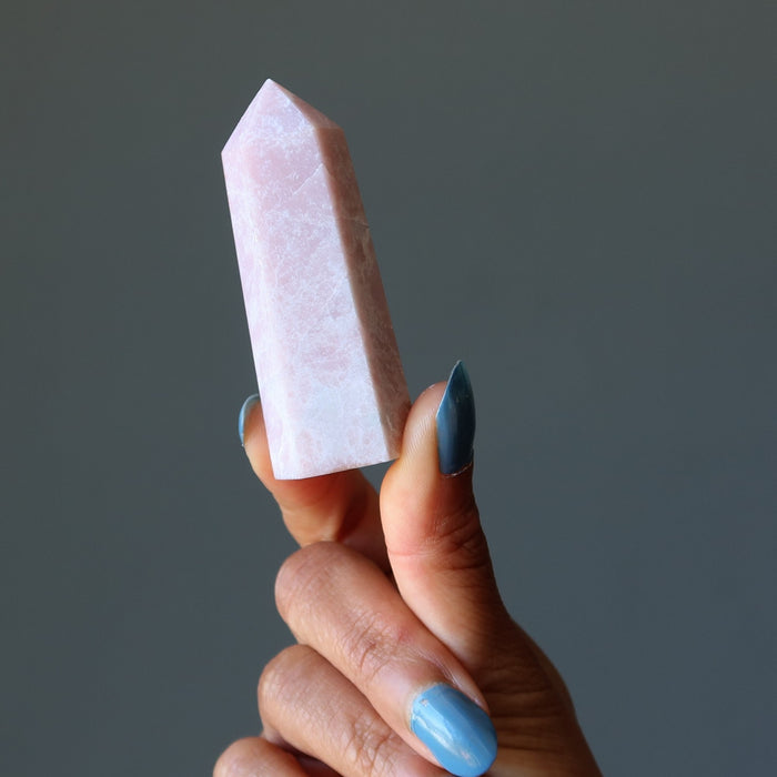 Hand holding a pink crystal opal against a gray background