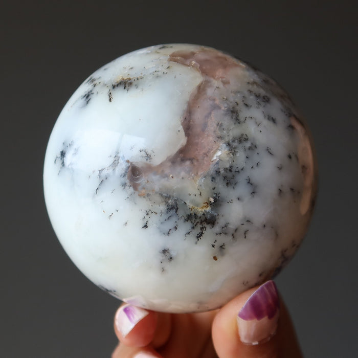 Marble-like opal held by a hand with pink nail polish against a dark background