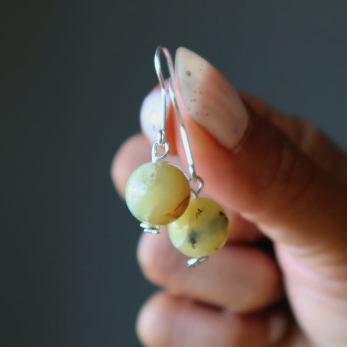 Hand holding a pair of yellow bead earrings against a dark background
