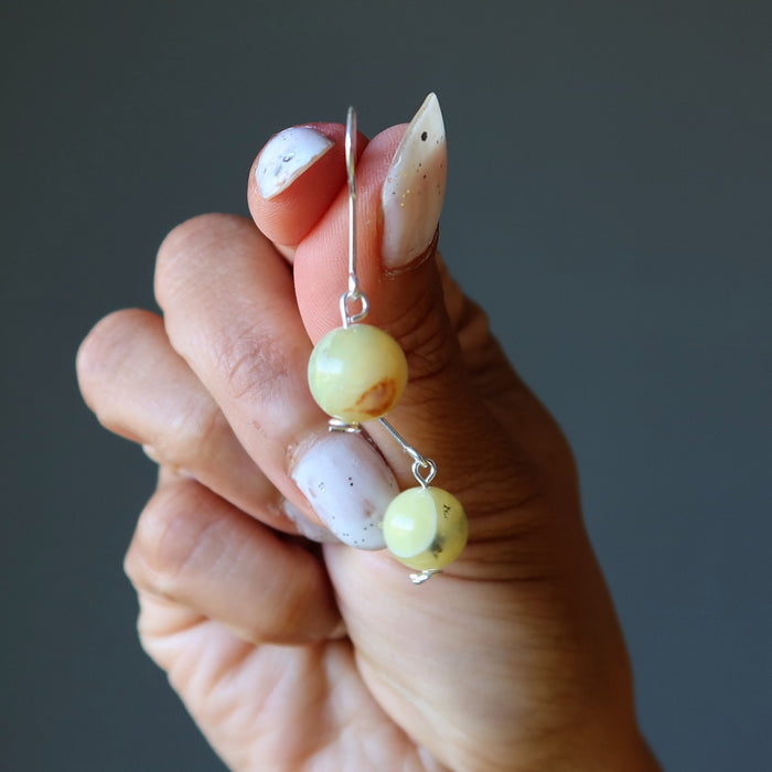 Hand holding a pair of opal earrings with yellow beads against a dark background