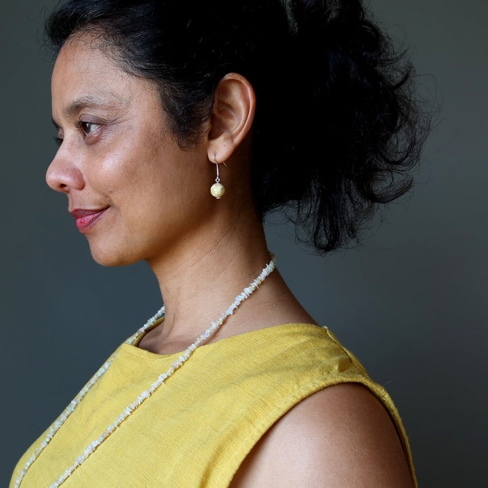 Woman wearing a yellow top and opal necklace against a gray background