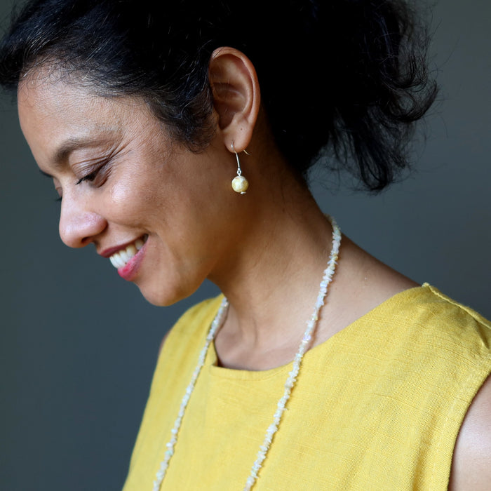 Woman wearing a yellow top and Opal necklace against a gray background