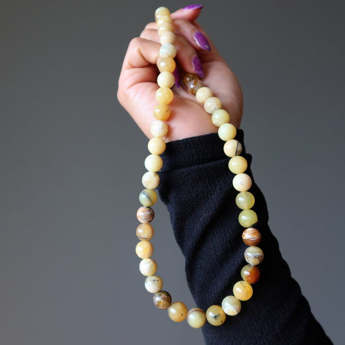 Hand holding a beaded Opal necklace against a gray background
