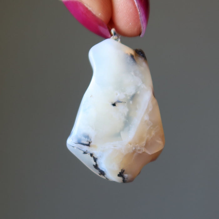 Polished Opal stone pendant held by a hand against a gray background