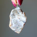 Raw stone Opal pendant held by a hand with pink nail polish against a gray background