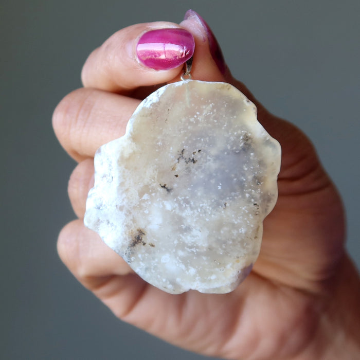 Hand holding a rough Opal crystal rock against a neutral background
