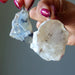 Raw Opal crystal pendants held by a hand with pink nail polish against a neutral background