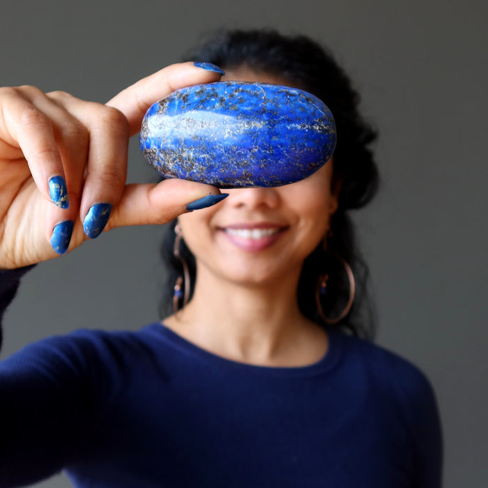 Woman holding a blue Lapis stone over her eyes against a gray background