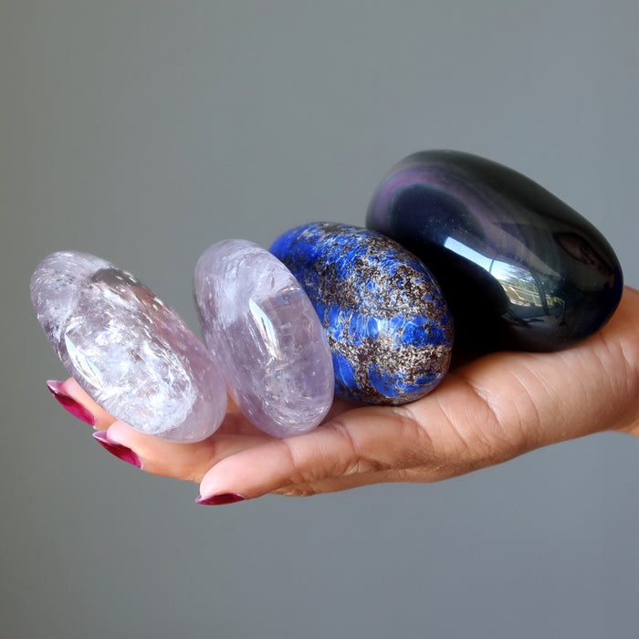 Hand holding four different colored stones against a gray background