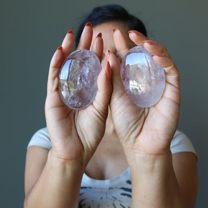 Person holding two Amethyst crystal ovals against a neutral background