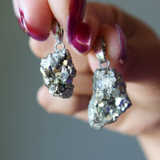 Geode-style Pyrite pendants held by a hand with purple nail polish against a neutral background