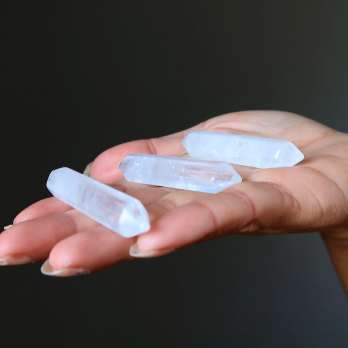 Hand holding three clear quartz doubleterminated crystal points against a dark background