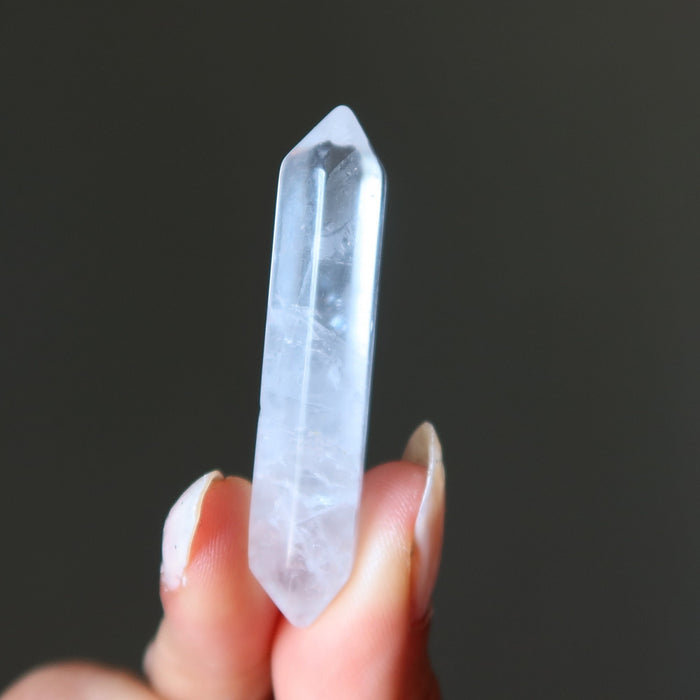 Clear quartz doubleterminated wand held between fingers against a dark background