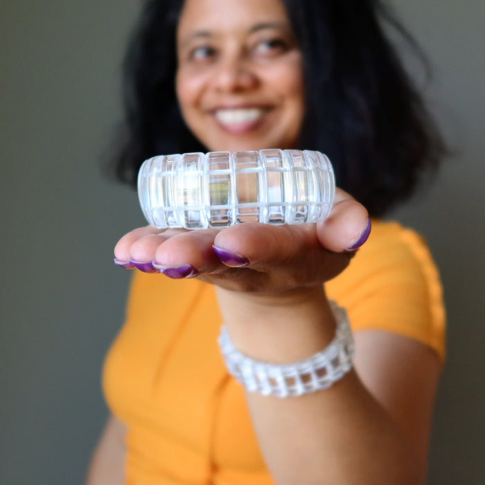 Person holding a Clear Quartz bracelet with a grid pattern, wearing an orange shirt.
