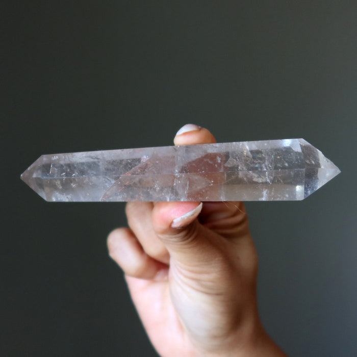 Hand holding a Clear quartz crystal wand against a dark background