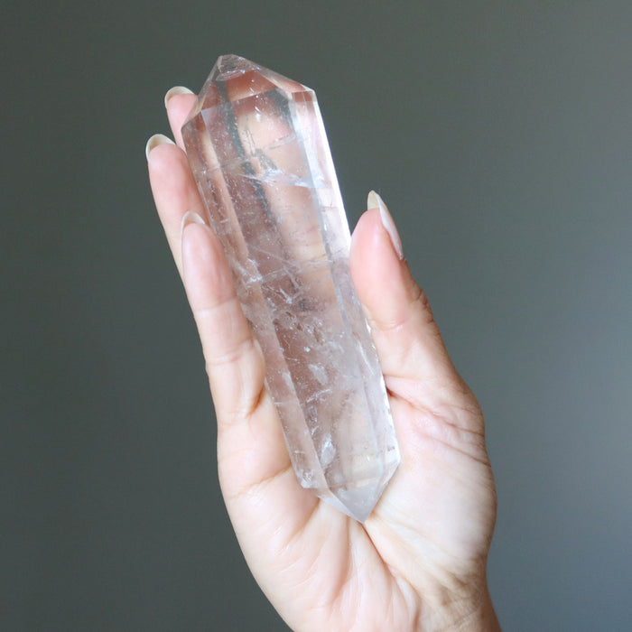 Hand holding a Clear quartz crystal wand against a dark background