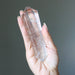 Hand holding a Clear quartz crystal wand against a dark background