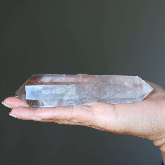 Clear quartz crystal wand held in a hand against a dark background