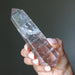 Clear quartz crystal wand held in a hand against a dark background