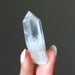 Clear lemurian quartz point crystal held in a hand against a dark background