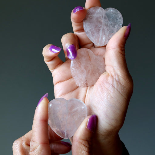 Heart-shaped Quartz crystals held in a hand with purple nail polish against a dark background