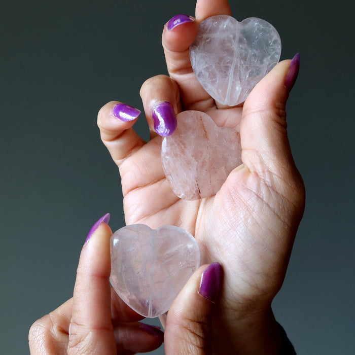 Heart-shaped Quartz crystals held in a hand with purple nail polish against a dark background