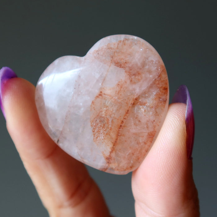 Heart-shaped Quartz stone held between fingers against a dark background